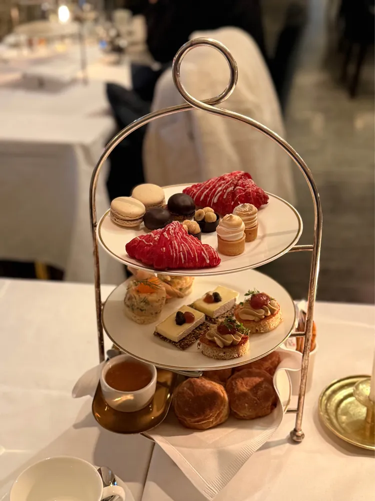 A three-tiered tray of food. From the bottom up, scones, tea sandwiches, and small desserts